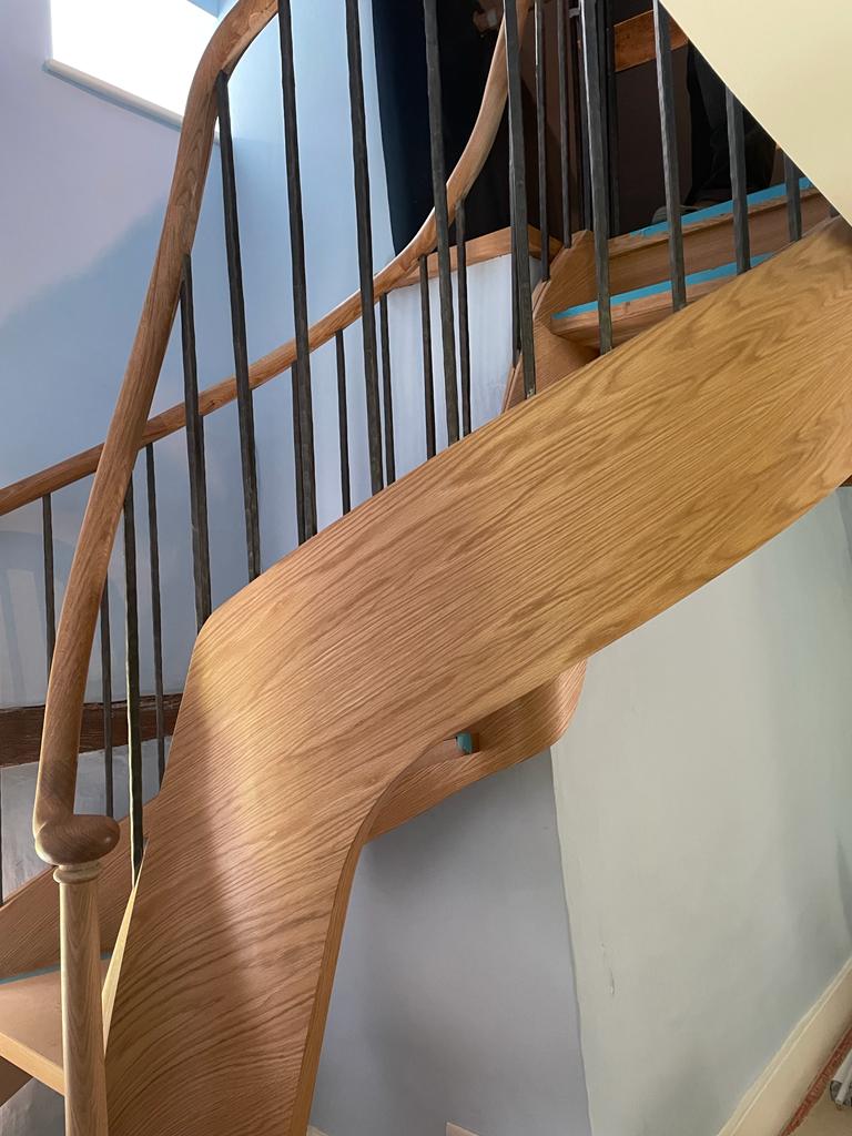 Oak fully helical closed string stair with continuous oak handrail, plain metal bar balustrade.