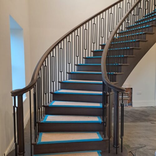 Stained Oak fully helical cut string staircase with metal balustrade and a continuous handrail being installed